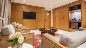 Un salon moderne doté d’un téléviseur à écran plat, de meubles en bois, d’un coin cuisine et d’un espace repas avec une table ronde.