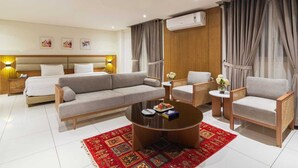 Une chambre d’hôtel moderne comprenant un grand canapé, un canapé plus petit, deux fauteuils, une table basse et un lit avec une tête de lit.