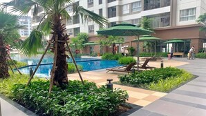 A modern outdoor pool area with lounge chairs, palm trees, and a building in the background.