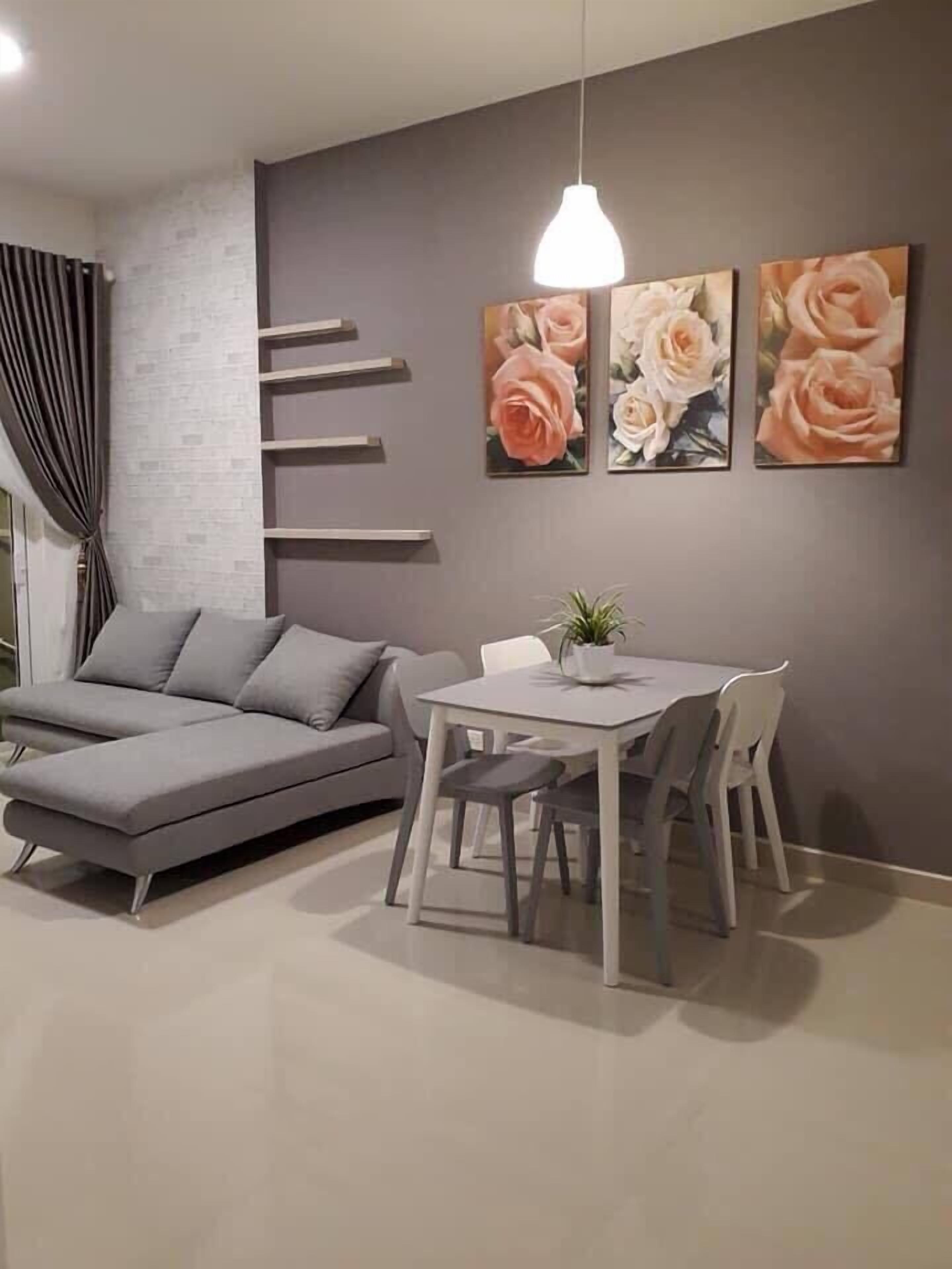 Ein modernes Wohnzimmer mit einem grauen Ecksofa, einem Esstisch mit vier Stühlen und drei an der Wand befestigten Rosenbildern.