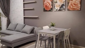 A modern living room with a grey sectional sofa, a dining table with four chairs, and three wall-mounted rose paintings.