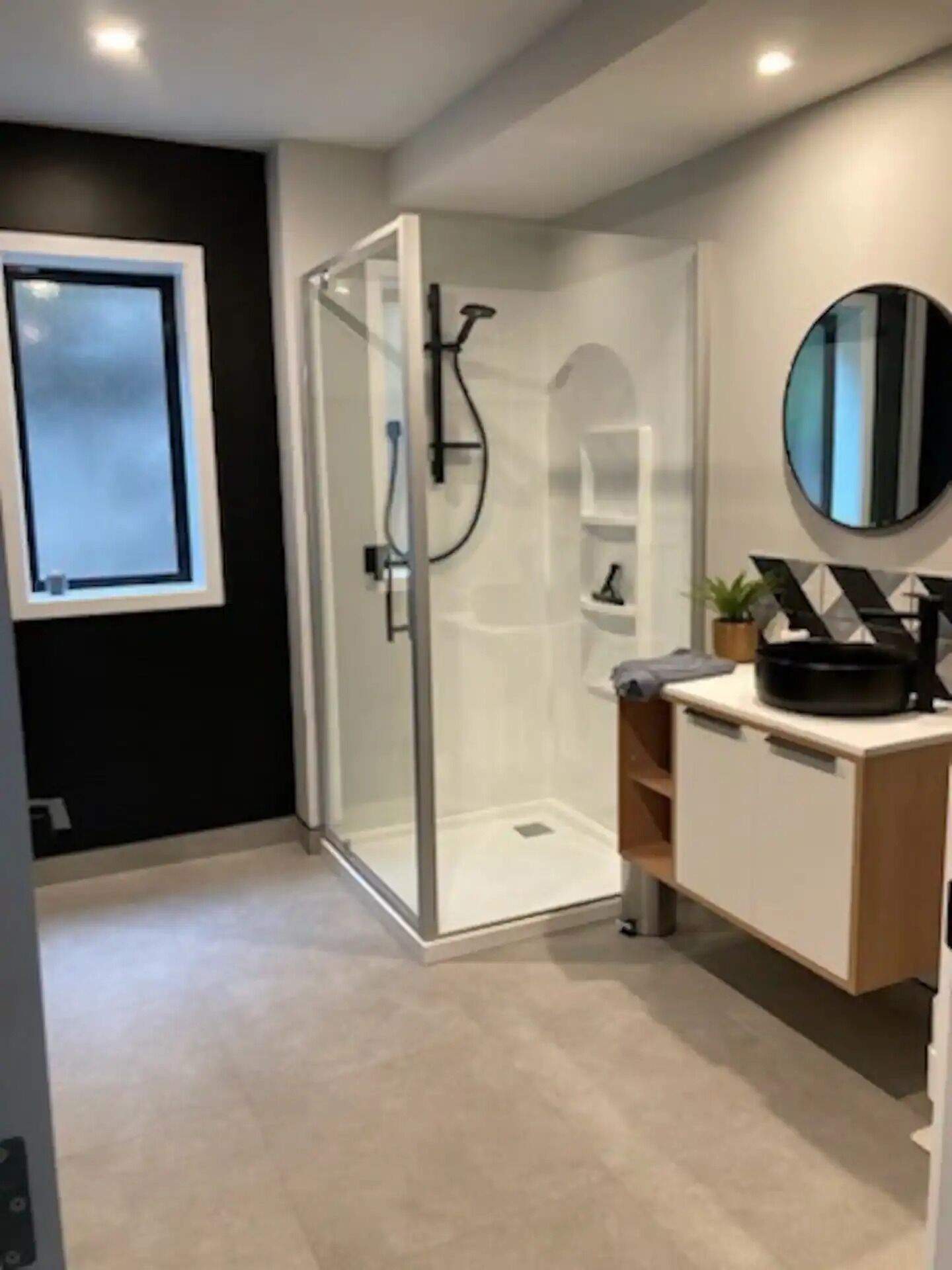 A modern bathroom with a glass shower enclosure, a large mirror, and a wooden vanity with a sink.