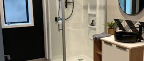 A modern bathroom with a glass shower enclosure, a large mirror, and a wooden vanity with a sink.