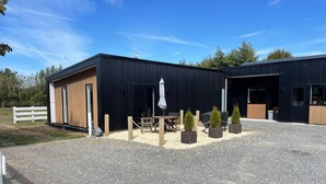 Een modern gebouw met een grindpad, houten omheining en een klein terras met een tafel en stoelen.