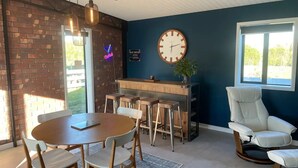 Een eetgedeelte met een ronde tafel, houten stoelen, een bar en een witte leren fauteuil.