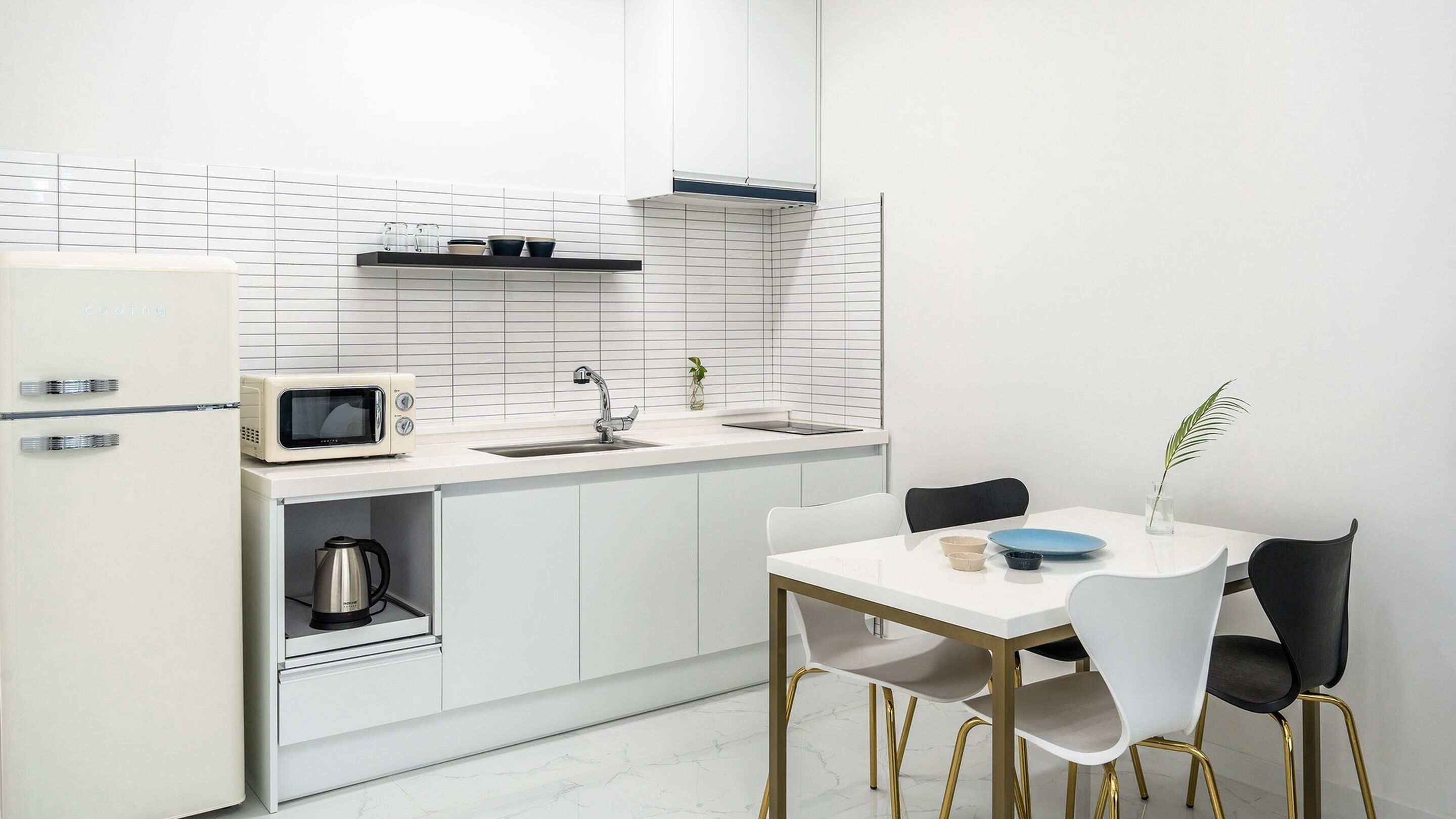 A modern kitchen with white cabinetry, a microwave, a kettle, and a dining table with chairs.
