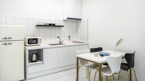 Uma cozinha moderna com armários brancos, micro-ondas, chaleira e uma mesa de jantar com cadeiras.