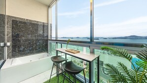 Un baño moderno con bañera, un balcón con paredes de vidrio y vistas al mar y a islas distantes.
