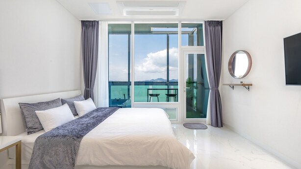 Una habitación de hotel moderna con una cama grande, un balcón con vistas al mar y un televisor de pantalla plana montado en la pared.