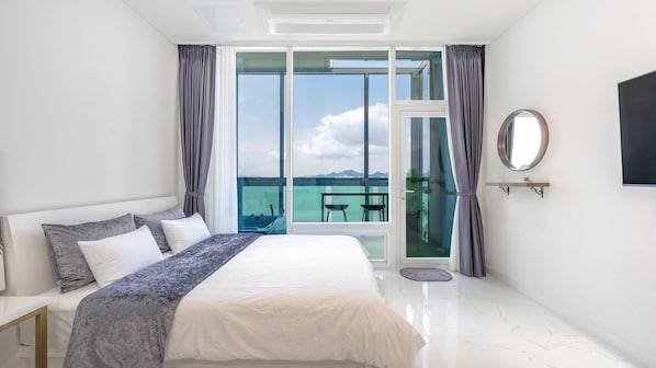 Een moderne hotelkamer met een groot bed, een balkon met uitzicht op zee en een flatscreen televisie aan de wand.