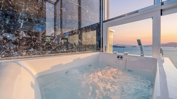 A bathtub with a view of the sea and mountains through a large window.