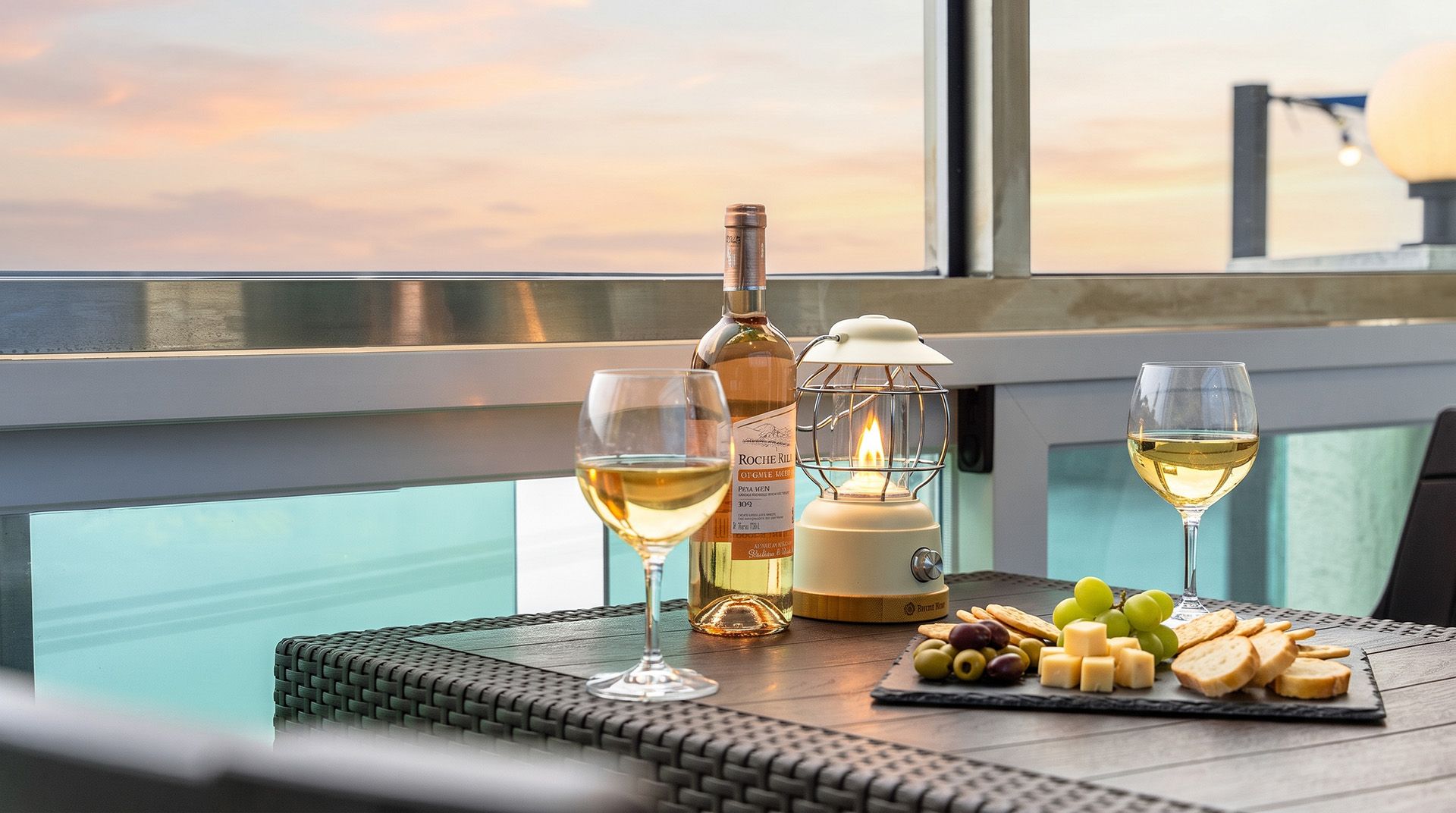 A table with a bottle of wine, two glasses, a candle, and a cheese board with grapes and crackers.