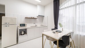 Moderni keittiö, jossa on valkoiset kodinkoneet, ruokapöytä tuoleineen ja näkymä ohuiden verhojen läpi.