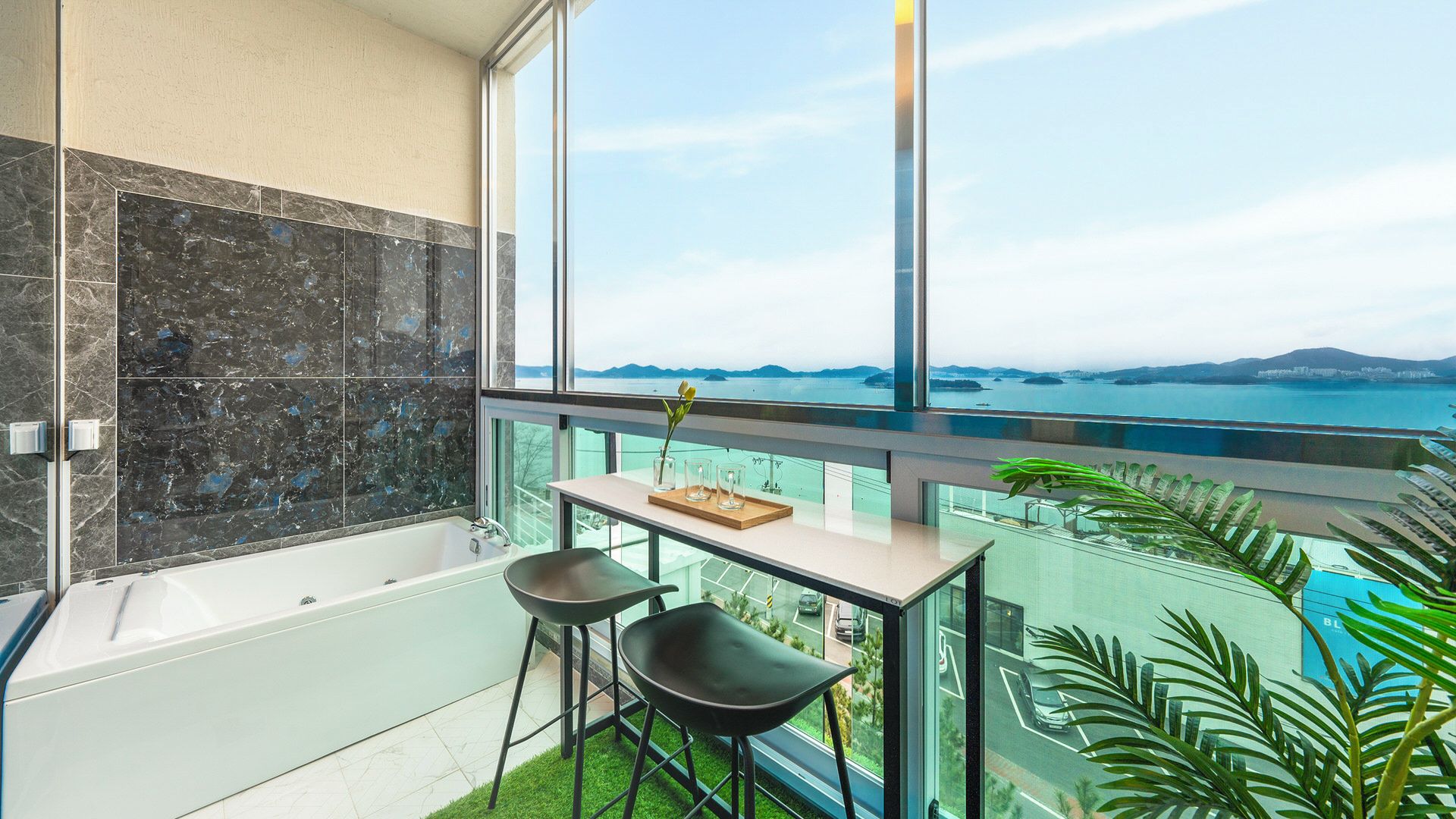 Un baño moderno con bañera, mampara de vidrio y un amplio ventanal con vista al mar.