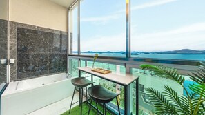 Un baño moderno con bañera, mampara de vidrio y un amplio ventanal con vista al mar.