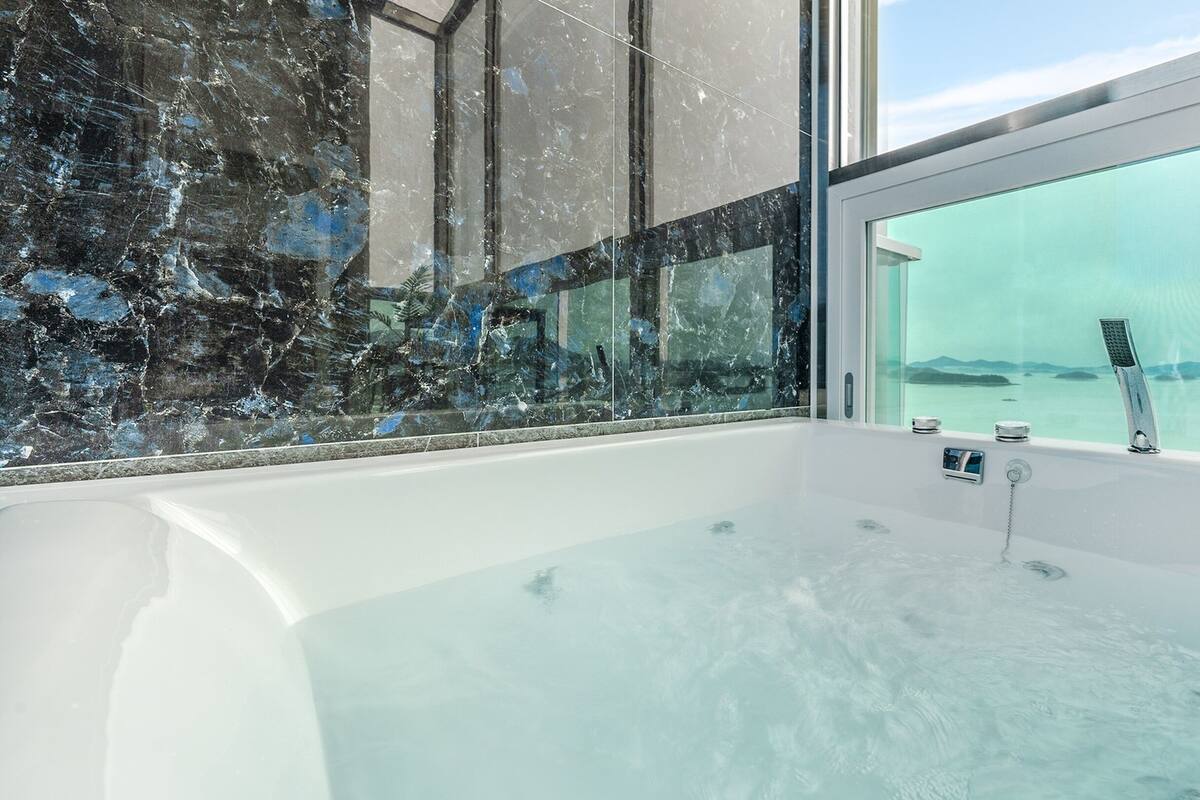 Een moderne badkamer met een ruime badkuip, een douchecabine van glas en uitzicht op zee.