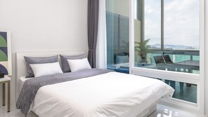 Een moderne slaapkamer met een groot bed, een nachtkastje en uitzicht op een balkon met een plant.