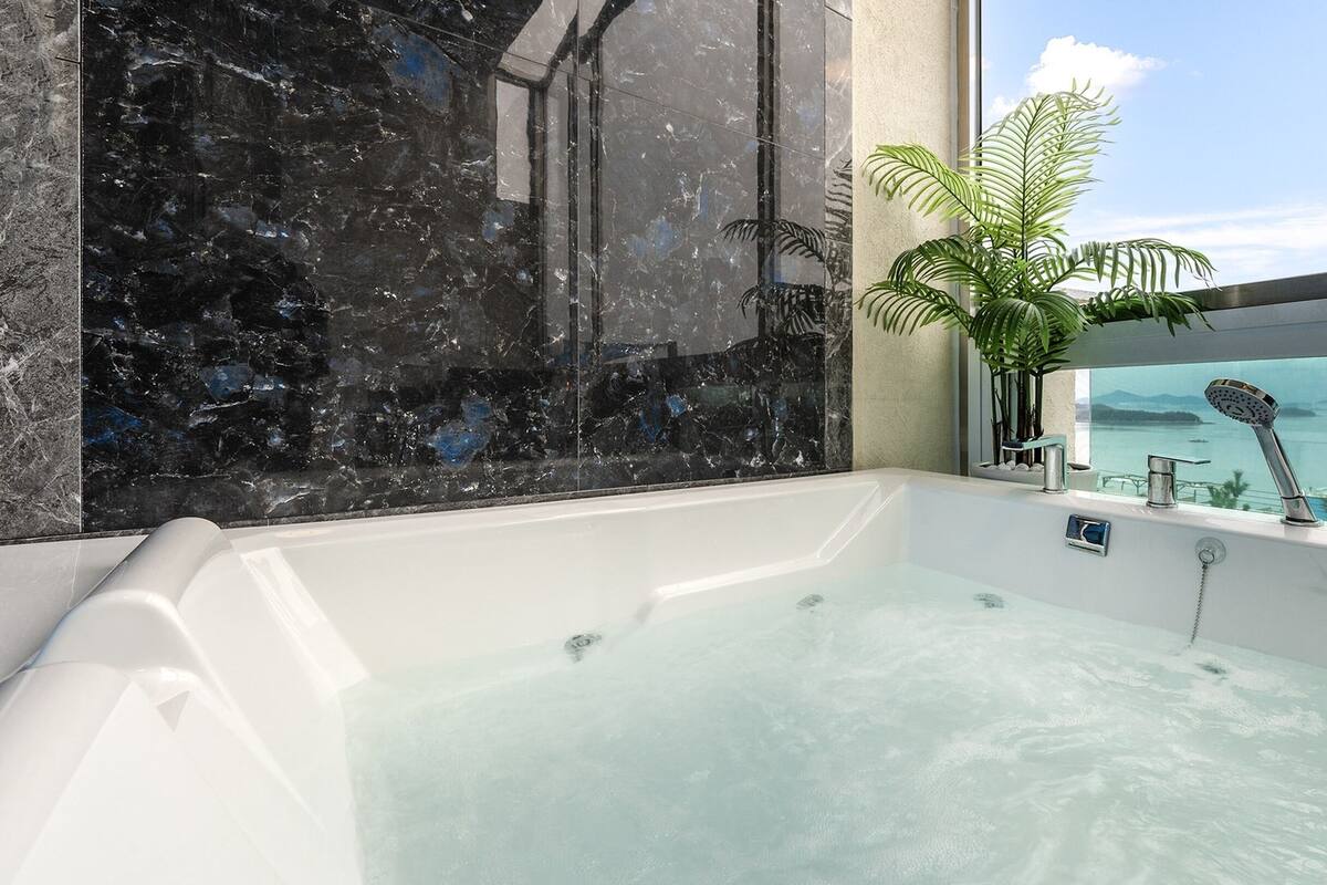 Een moderne badkamer met een groot bad, een marmeren wand en uitzicht op zee.