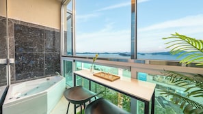 Uma casa de banho moderna com banheira, cabine de chuveiro em vidro e vista para um corpo de água através de amplas janelas.