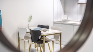 Uma sala de jantar moderna com uma mesa branca, cadeiras preto e branco e uma pequena planta.