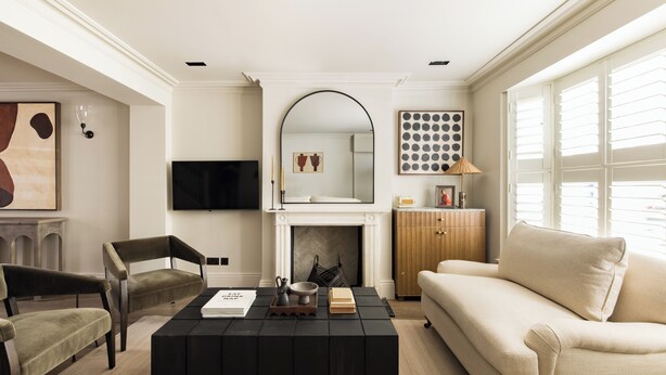 A modern living room with a fireplace, a sofa, a coffee table, and a TV. - Welcome to our newly renovated 4-bedroom, 2-bathroom retreat in the heart of Kensington. Warm tones, plush textures, and elegant touches create a serene space. Unique artworks and opulent accents add character throughout. Perfect getaway starts here. (London)