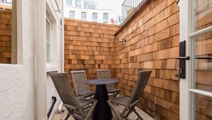 A small patio area with a round table and four chairs, surrounded by wooden paneling. - Welcome to our newly renovated 4-bedroom, 2-bathroom retreat in the heart of Kensington. Warm tones, plush textures, and elegant touches create a serene space. Unique artworks and opulent accents add character throughout. Perfect getaway starts here. (London)