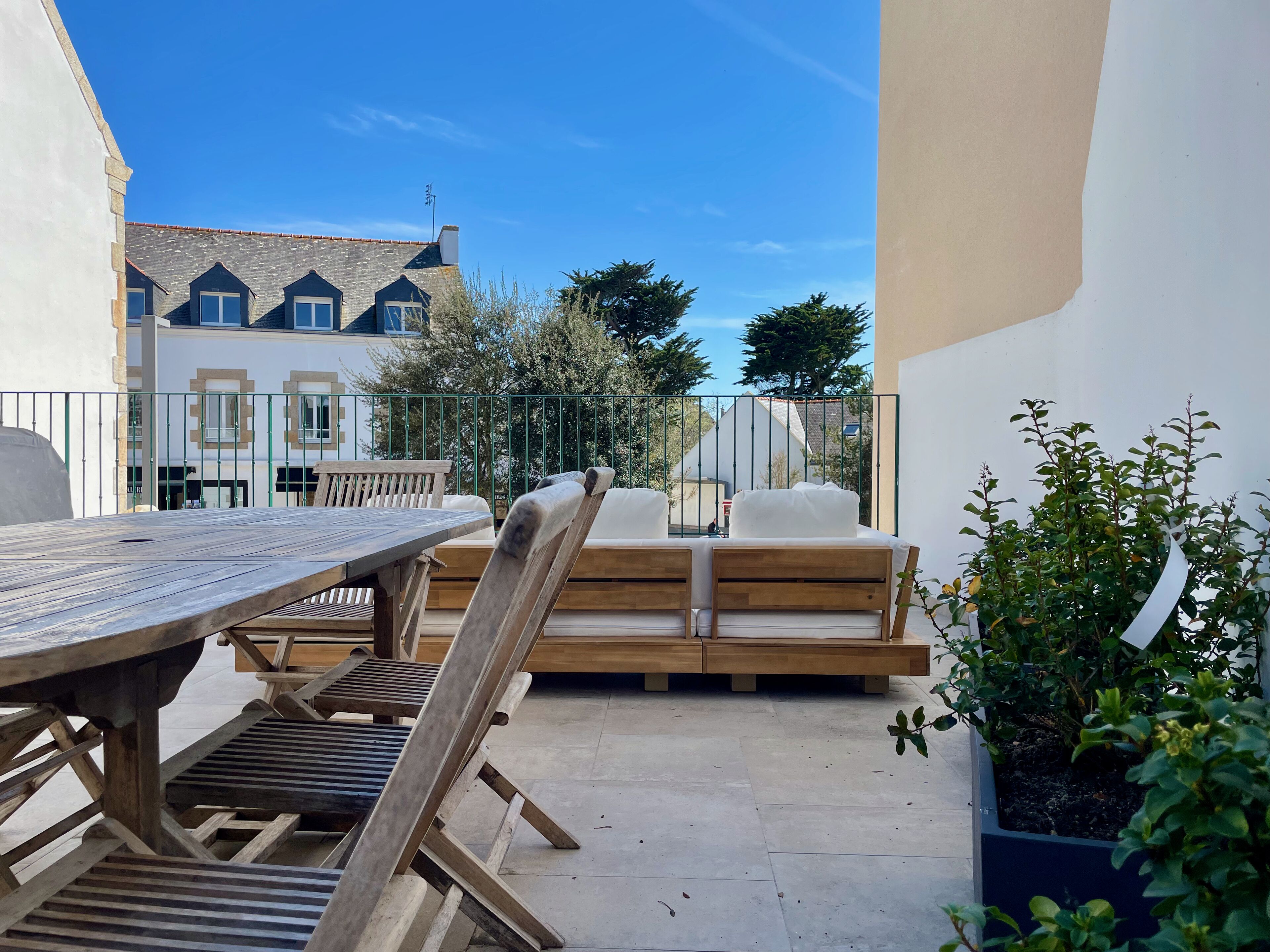 A patio with a wooden table and chairs, a sofa, and a potted plant.