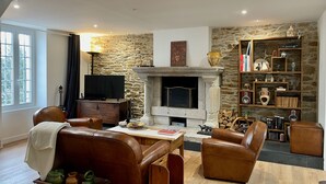 A cozy living room with a stone fireplace, leather furniture, and a bookshelf filled with books and decorative items.