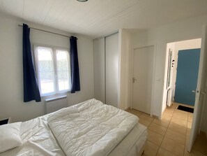 Ein Schlafzimmer mit Bett, einem Vorhangfenster, einem Heizkörper und einer Tür zu einem anderen Raum.