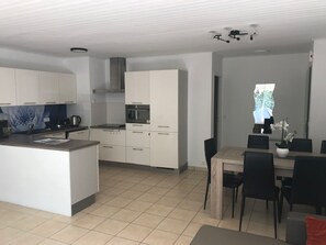 Eine moderne Küche mit weißen Schränken, einer zentralen Kochinsel und einem Essbereich mit Holztisch und Stühlen.