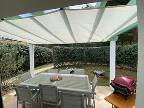 Eine überdachte Terrasse mit Tisch und Stühlen, einem Grill und einem gepflegten Garten.