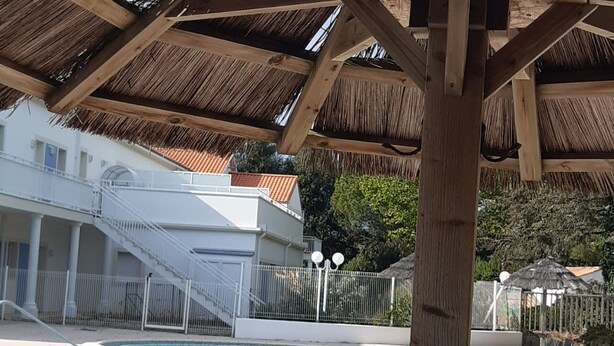 Ein Schwimmbecken mit gefliestem Rand, eine Holzzahl und ein weißes Gebäude mit einer Treppe.