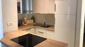 Eine moderne Küche mit weißen Schränken, einer schwarzen Induktionskochplatte, einer Edelstahl-Dunstabzugshaube, einer integrierten Spüle und einem weißen Kühlschrank.