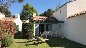 Ein kleiner, privater Garten mit einer Terrasse, inklusive Tisch und Stühlen, umgeben von weißen Wänden und einem Ziegeldach.