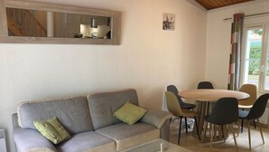 Ein Wohnzimmer mit grauem Sofa, einem Glastisch und einem Essbereich mit rundem Tisch und Stühlen.