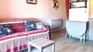A small, cozy room with a bed, a small table, a radiator, and a shelf with various items. - Lovely T2 in Collioure, direct beach access, air conditioning, private parking (Collioure)