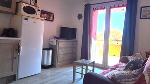 A compact living space with a kitchenette, a television, a sofa, and a sliding glass door leading to an outdoor area. - Lovely T2 in Collioure, direct beach access, air conditioning, private parking (Collioure)