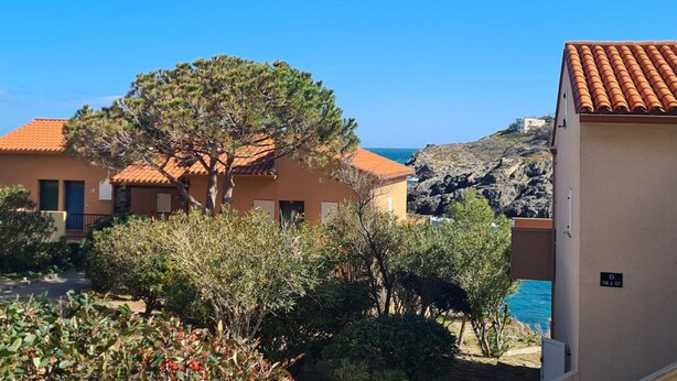 A coastal building with a tiled roof, surrounded by greenery and a clear view of the sea. - Lovely T2 in Collioure, direct beach access, air conditioning, private parking (Collioure)