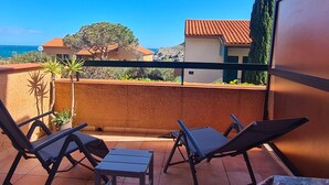 A balcony with two lounge chairs and a small table, overlooking a coastal area with houses and a clear blue sky. - Lovely T2 in Collioure, direct beach access, air conditioning, private parking (Collioure)