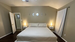Une chambre avec un grand lit, deux tables de chevet avec des lampes, une porte et un mur décoré avec les différentes phases de la lune.