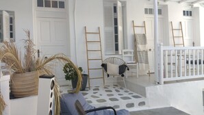 Un interior blanco con suelo de piedra, una silla de madera, una escalera y una planta en maceta.