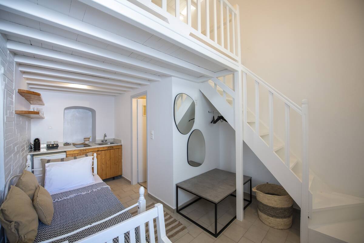 A bedroom with a bed, bedside table, and a large mirror. There is a staircase leading to an upper level.