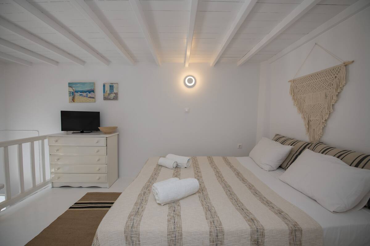 A bedroom with a bed, a TV on a dresser, and a wall-mounted macrame piece.