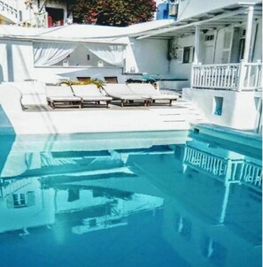 Zona de piscina con sillones de descanso y un área de estar techada.