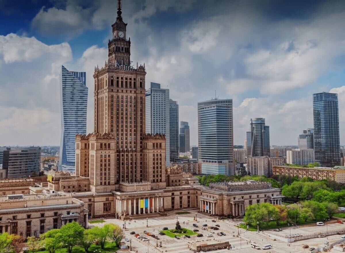 Ein historisches Gebäude mit einem Uhrturm, umgeben von modernen Wolkenkratzern und einem zentralen Platz mit Bäumen und einer Fontäne.