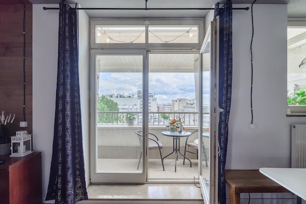 A balcony with a table and chairs, a view of the cityscape, and a door with patterned curtains.