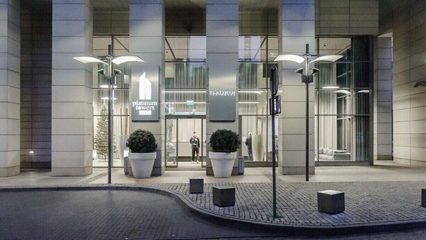 A modern building entrance with a glass facade, large potted plants, and a sign reading "Platinum Towers." - Apartment in Platinum Tower FV in Warsaw (Warszawa)