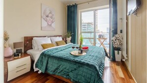 A bedroom with a bed, a nightstand, a TV, a window with curtains, and a balcony with a view. - Apartment in Platinum Tower FV in Warsaw (Warszawa)