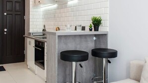 Une cuisine moderne avec des carreaux blancs, une porte sombre et deux tabourets de bar noirs.