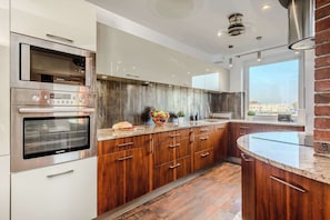 A modern kitchen with built-in appliances, wooden cabinetry, and a large window providing a view.